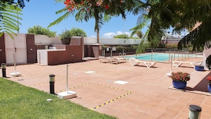 Zona junto a la piscina con sillones de descanso, piscina y jardín cercado.
