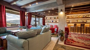 A cozy living area with a sofa, a dining table, and a bar with shelves of bottles. - La Noi Guesthouse (Grevena)