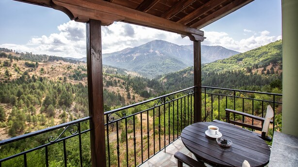 A wooden balcony with a table and bench, overlooking a mountainous landscape. - La Noi Guesthouse (Grevena)
