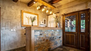 A reception area with a stone wall, wooden counter, framed artwork, and a wooden door with glass panels. - La Noi Guesthouse (Grevena)