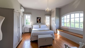 A bedroom with a bed, a chest of drawers, a bench, a radiator, and a window with a view of greenery. - Serene Seaside Bliss - Lush & Secluded Garden Oasis (Kalamata)