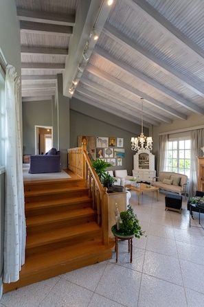 A spacious living area with a staircase, a chandelier, and a variety of furniture including a sofa, armchair, and a wooden coffee table. - Serene Seaside Bliss - Lush & Secluded Garden Oasis (Kalamata)