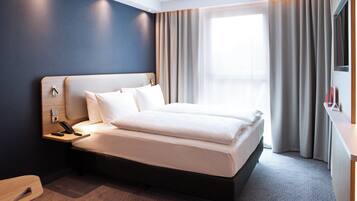 Ein modernes Hotelzimmer mit einem großen Bett, einem Nachttisch mit Telefon und einem Fenster mit Vorhängen.