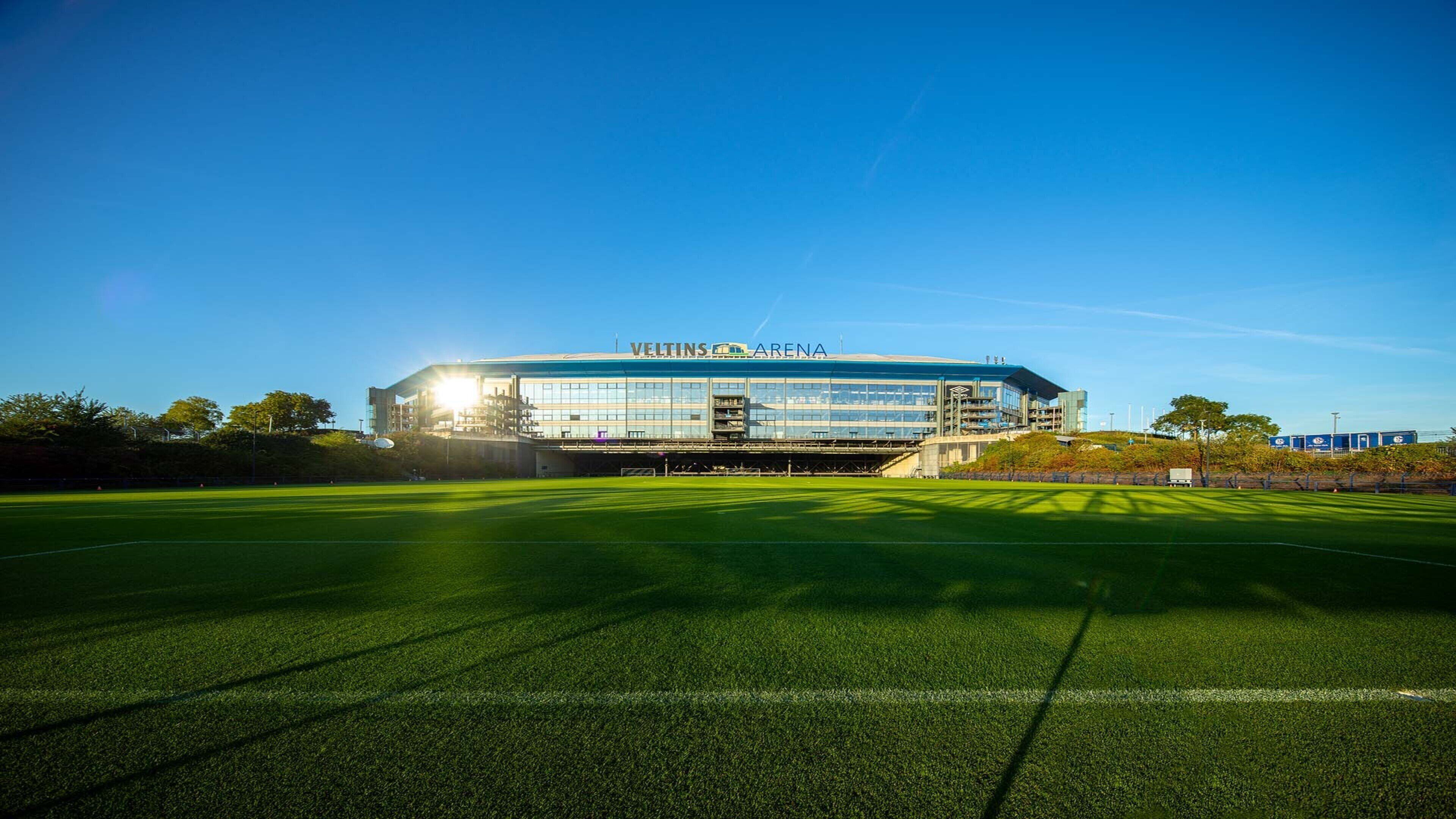 A modern sports stadium with a large, open field in front.