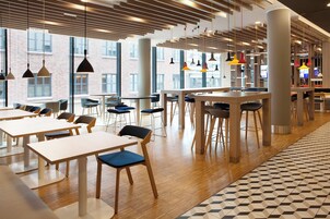 A modern cafe with wooden tables and chairs, large windows, and hanging pendant lights.