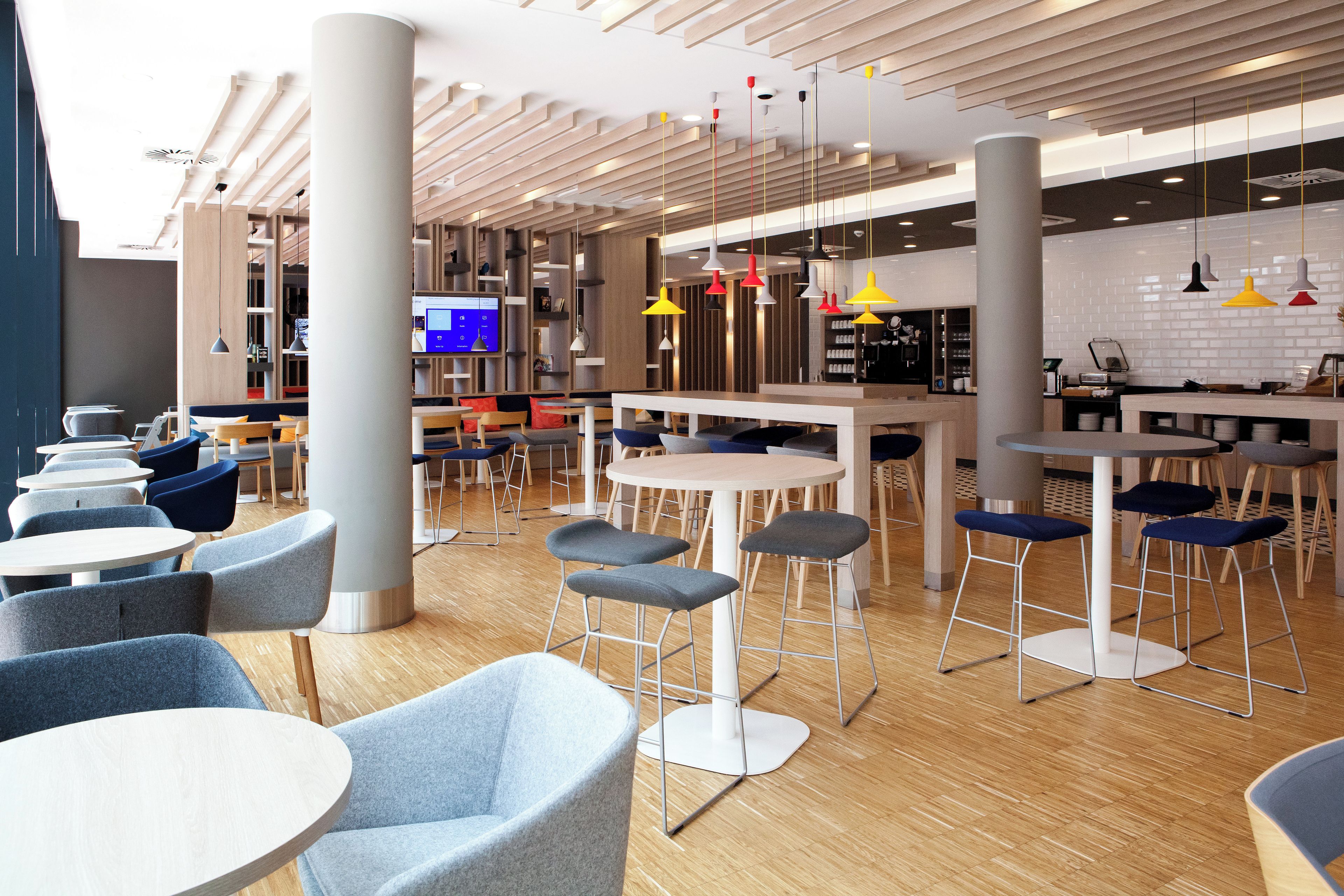A modern interior with round tables and bar stools, a television screen, and a kitchen area.