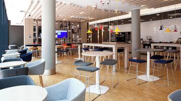 A modern interior with round tables and bar stools, a television screen, and a kitchen area.