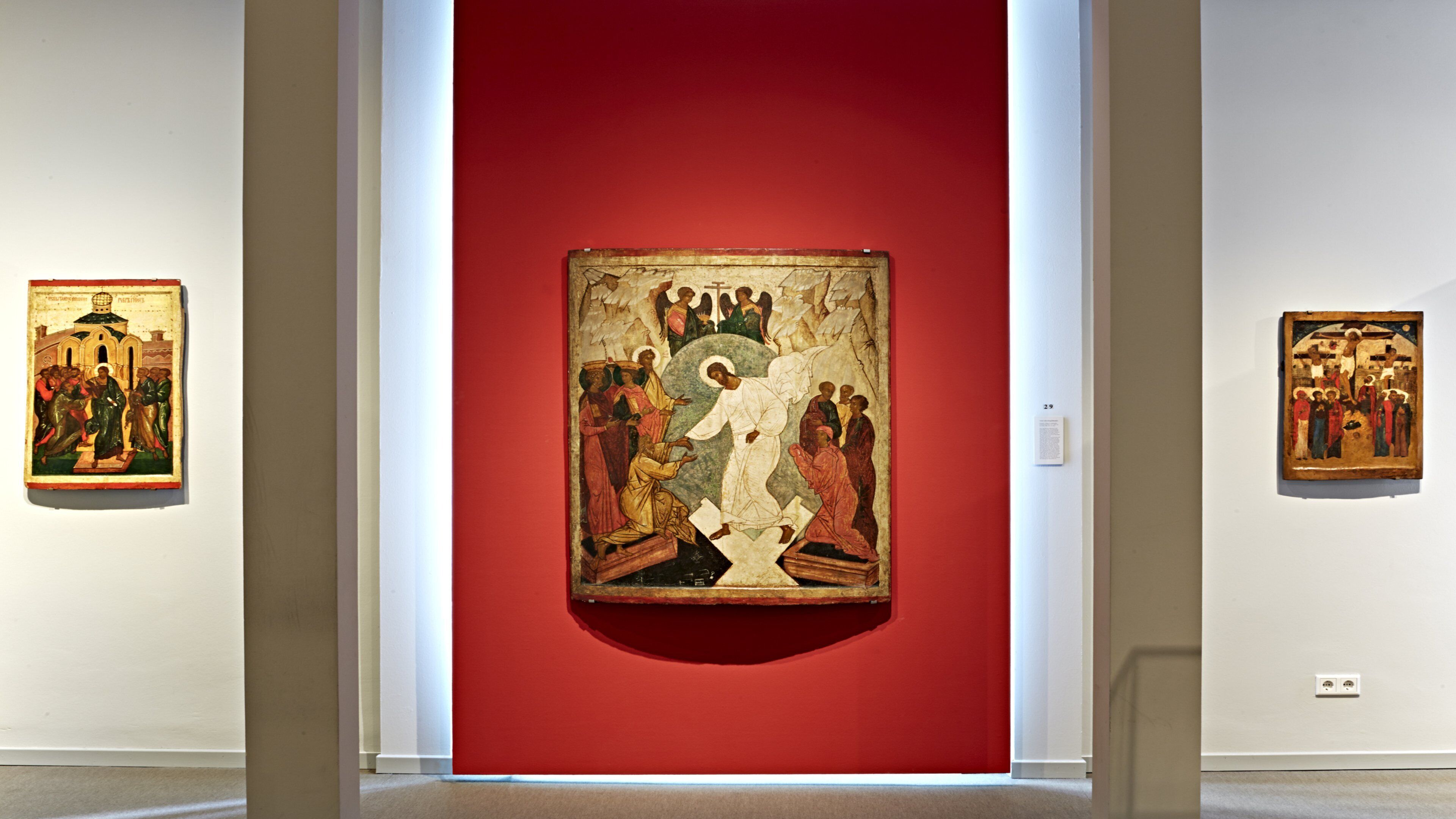 Eine Galerie mit drei gerahmten Kunstwerken an weißen Wänden, ein großes zentrales Werk und zwei kleinere daneben.