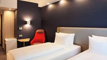 Ein Hotelzimmer mit einem Bett, einem roten Sessel, einem Nachttisch und einer Wandleuchte.