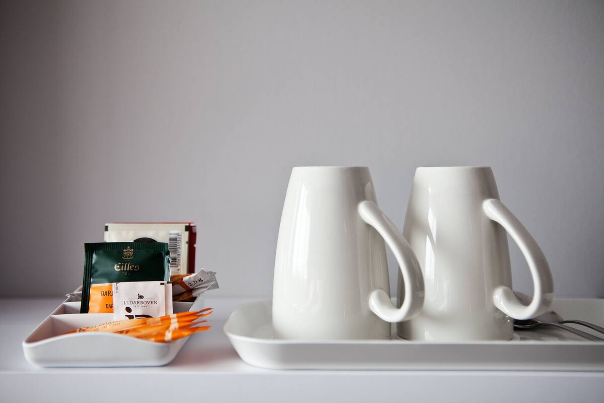 Two white ceramic mugs on a white tray, with a plate of orange and white items beside them.