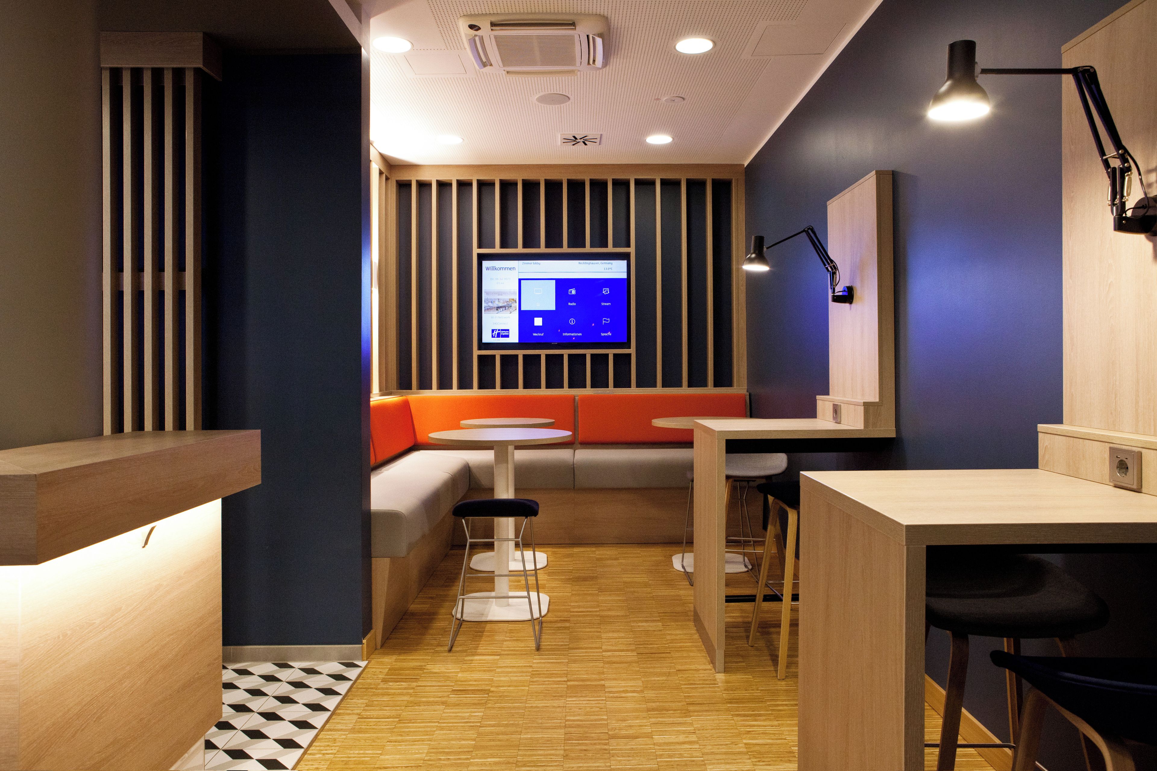 Un interior moderno con una zona de estar, mesas y una pantalla digital.