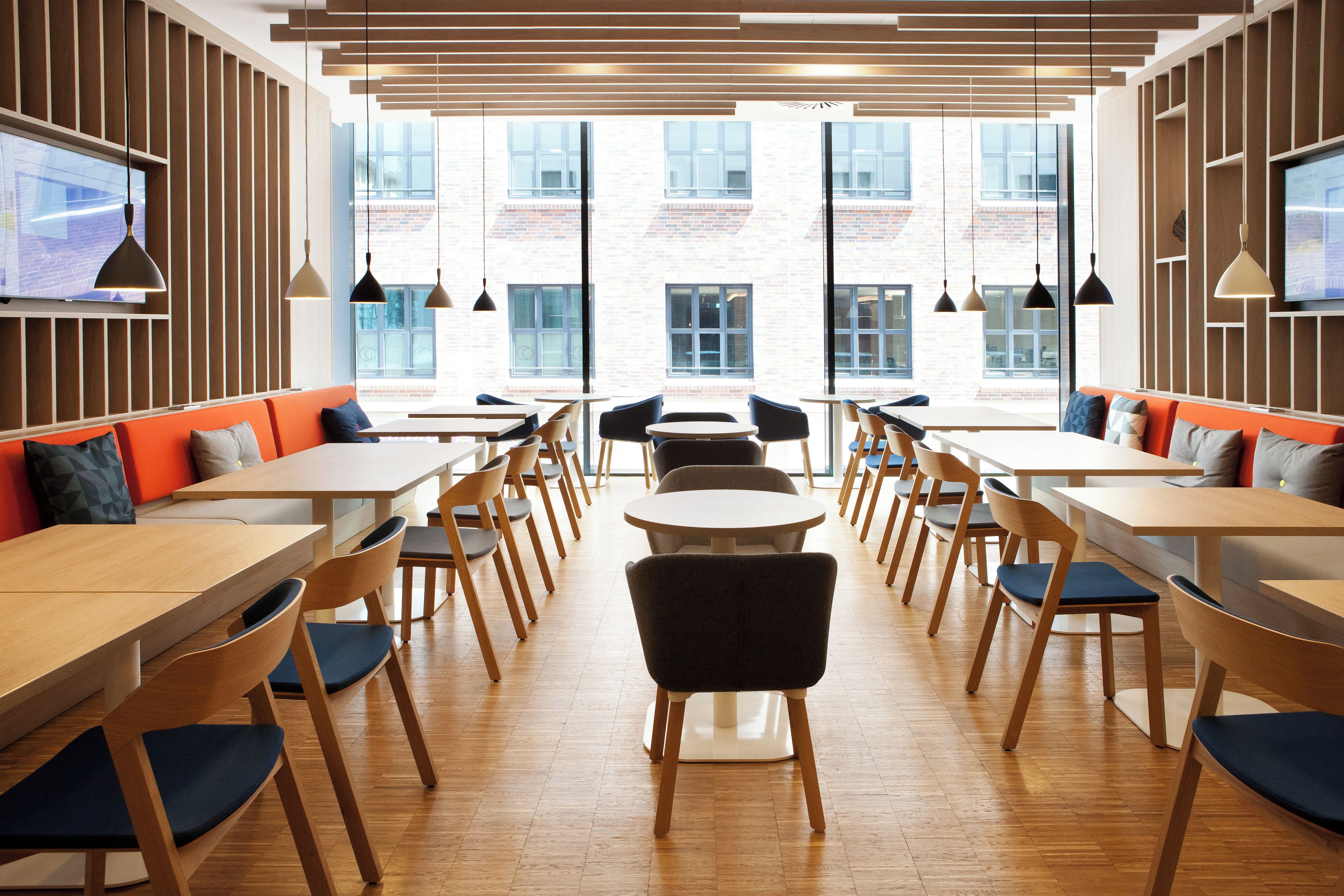 Ein modernes Interieur mit Holztischen und -stühlen, einer Ziegelwand und großen Fenstern.