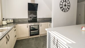 A modern kitchen with white cabinetry, a built-in oven, a black range hood, and a wall-mounted clock. - 26 Hycemoor Way (Millom)