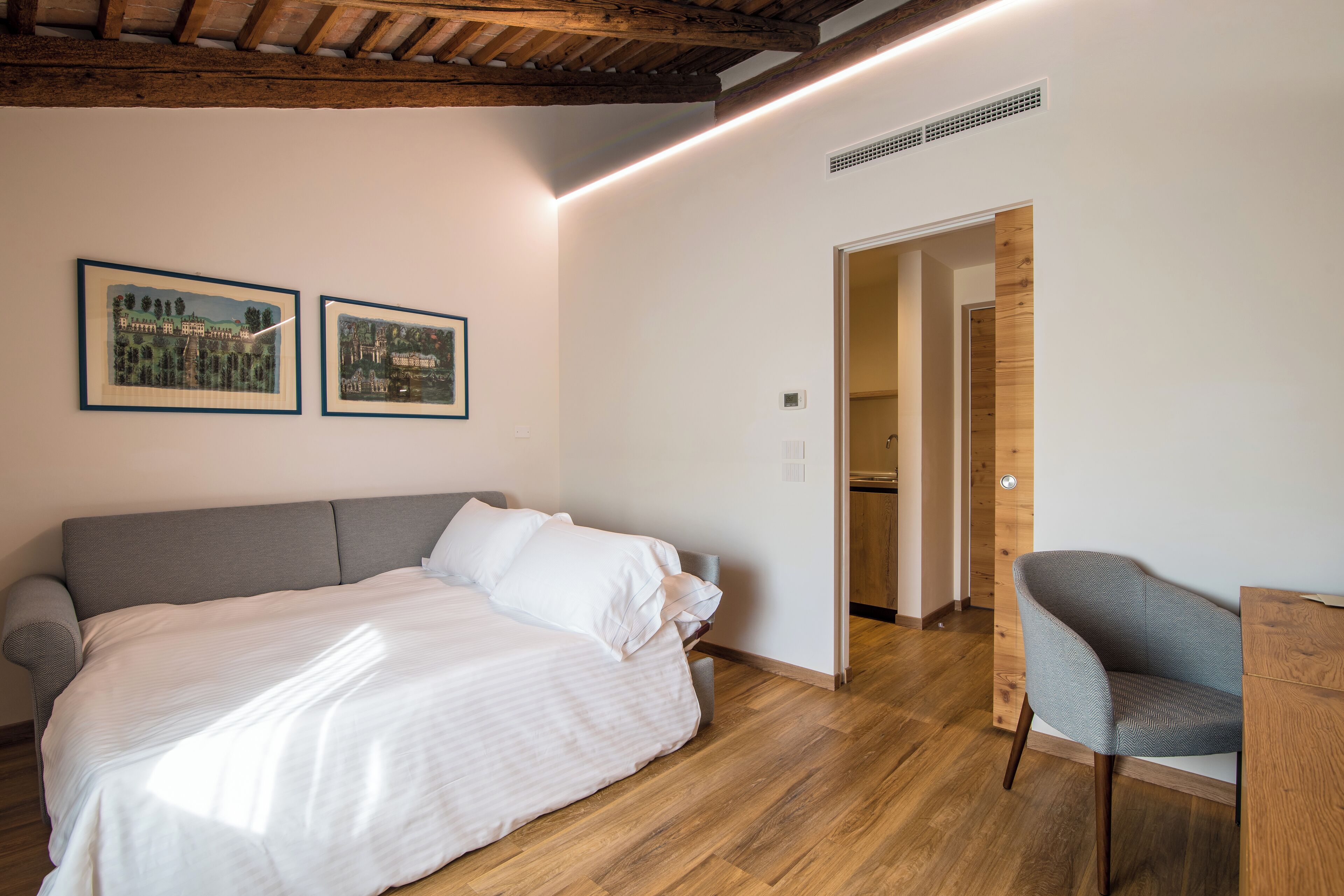 Un dormitorio con una cama, una silla y dos cuadros en la pared.