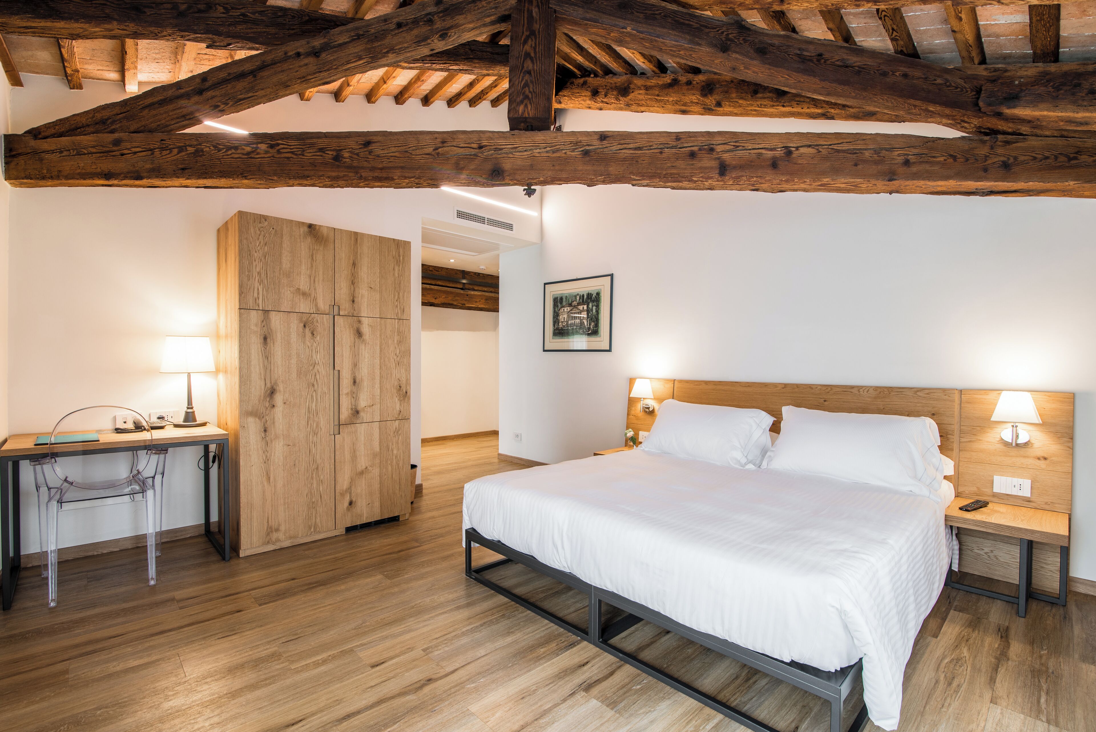 A bedroom with a wooden ceiling, a bed with white bedding, a desk with a chair, and a wardrobe.