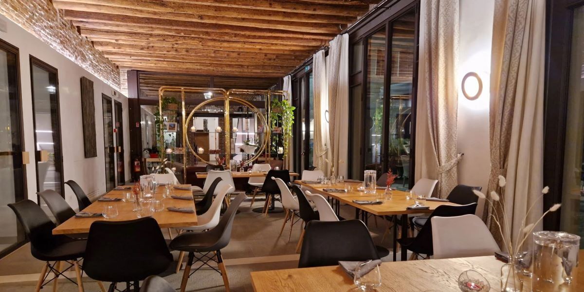 A restaurant with wooden tables and chairs, large windows, and a modern interior design.