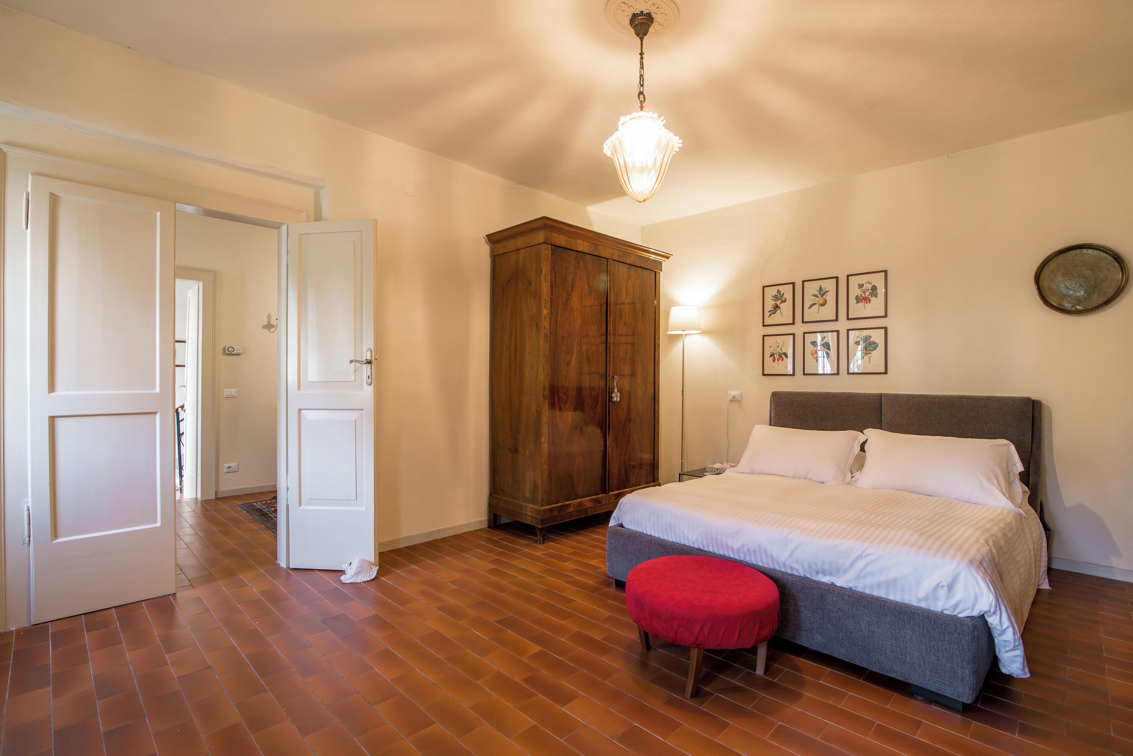 A bedroom with a bed, a wooden wardrobe, a red bench, and a chandelier.