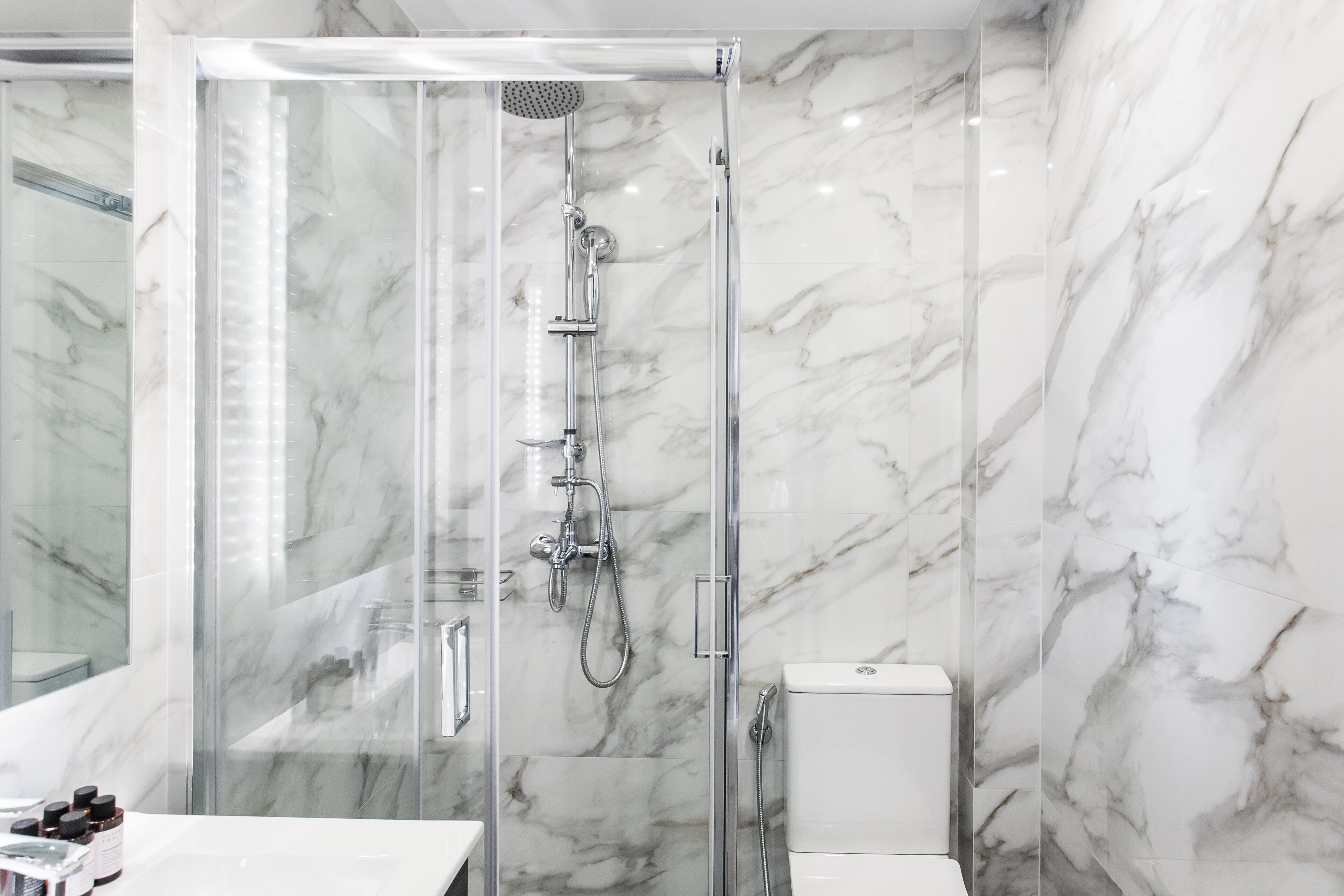 Un bagno moderno con doccia vetrata, pareti in marmo e lavandino bianco.
