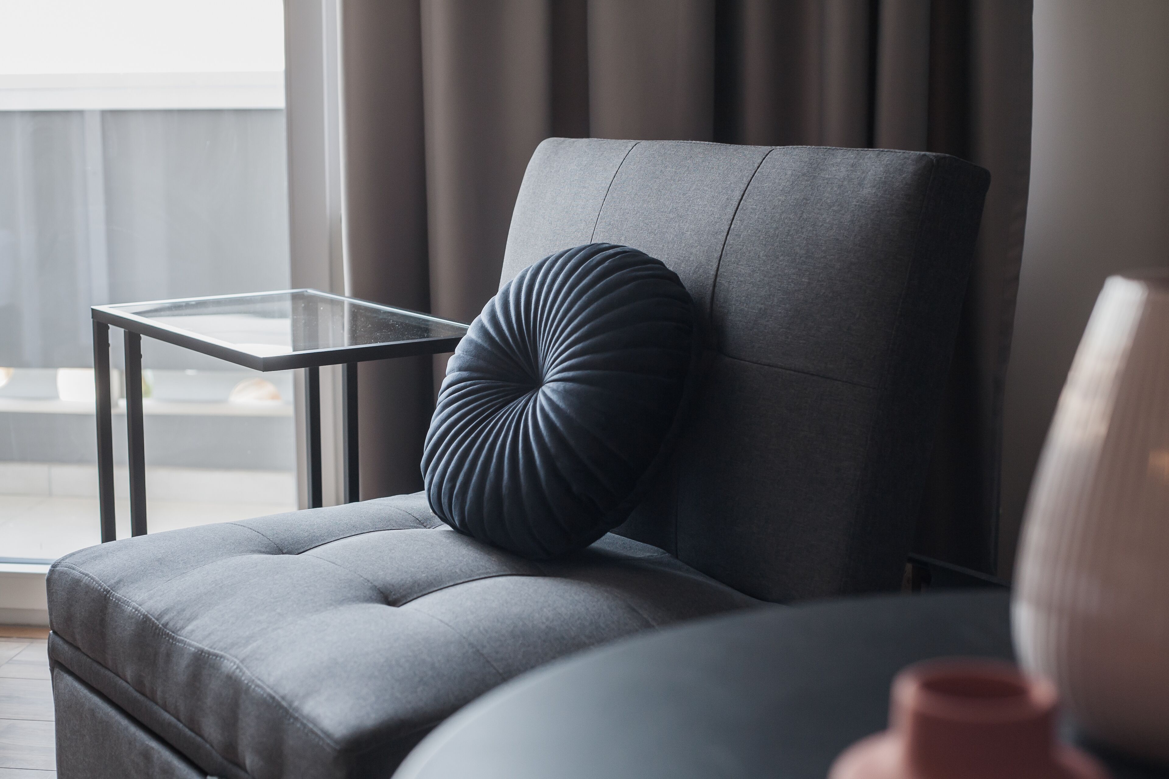 A modern living room with a grey sofa, a glass coffee table, and a dark grey pillow.