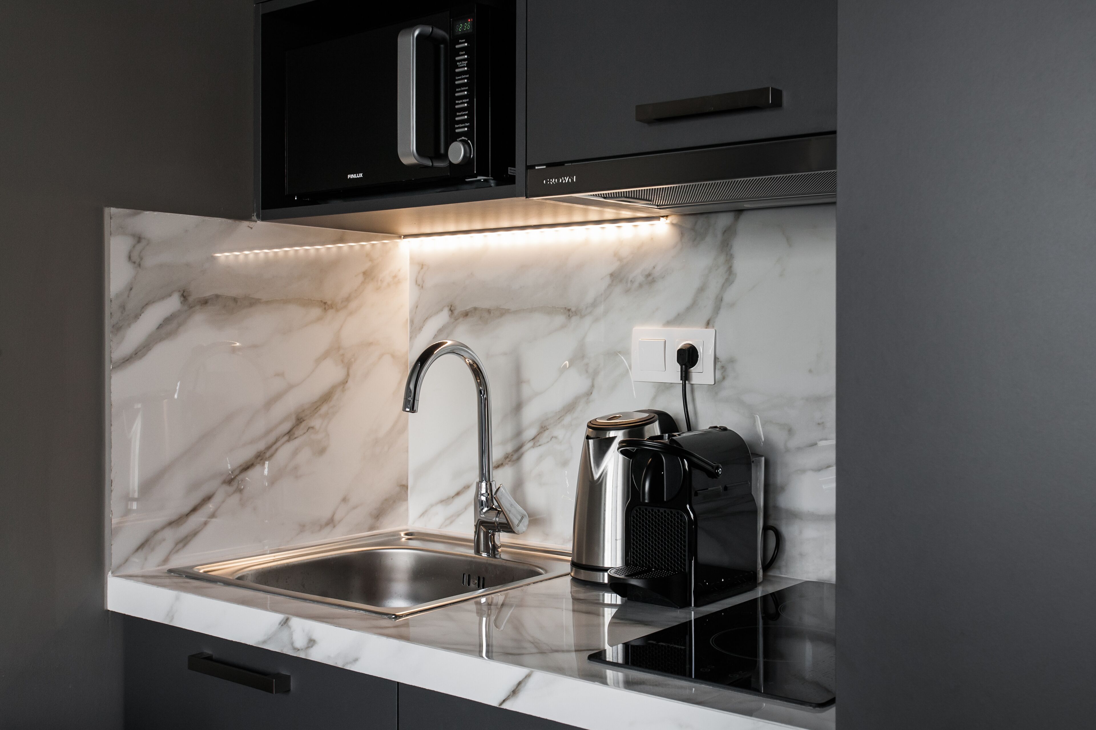 A modern kitchen with a marble countertop, stainless steel sink, and a coffee maker.