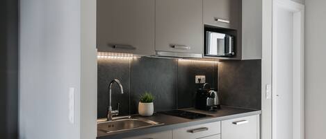 Una cocina moderna con microondas integrado, pileta de acero inoxidable y una pequeña planta en maceta.