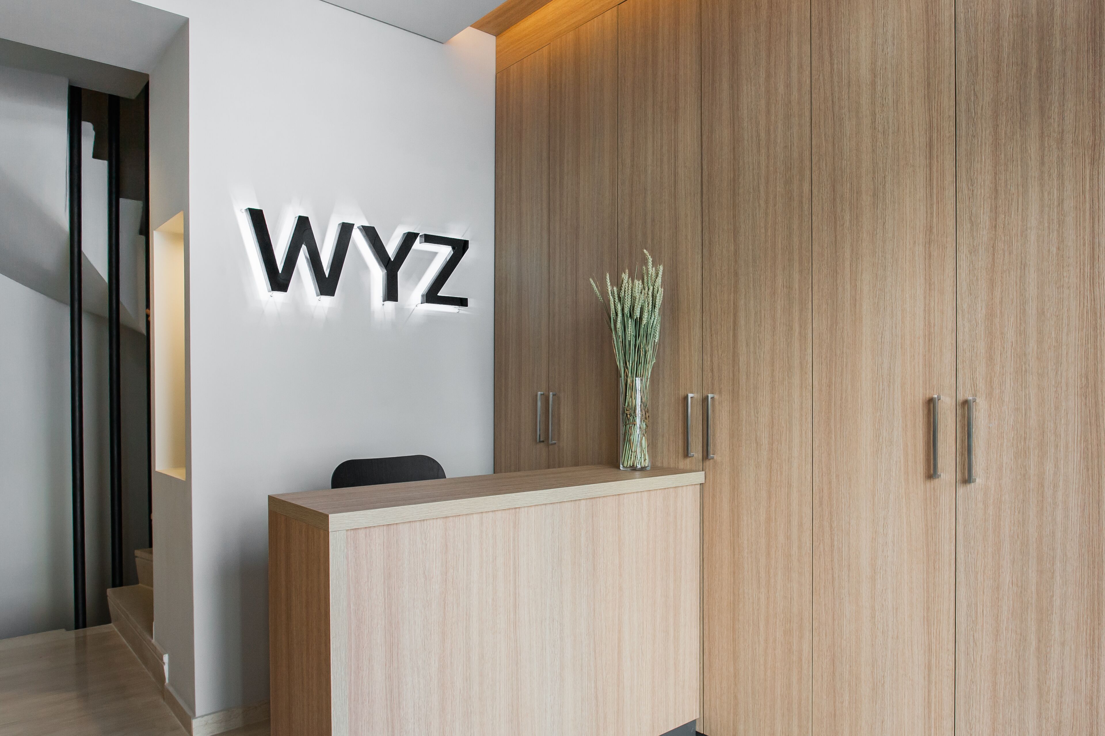 A reception desk with a light wood finish, a wall-mounted sign reading "WYZ", and a vase with dried plants on the counter.