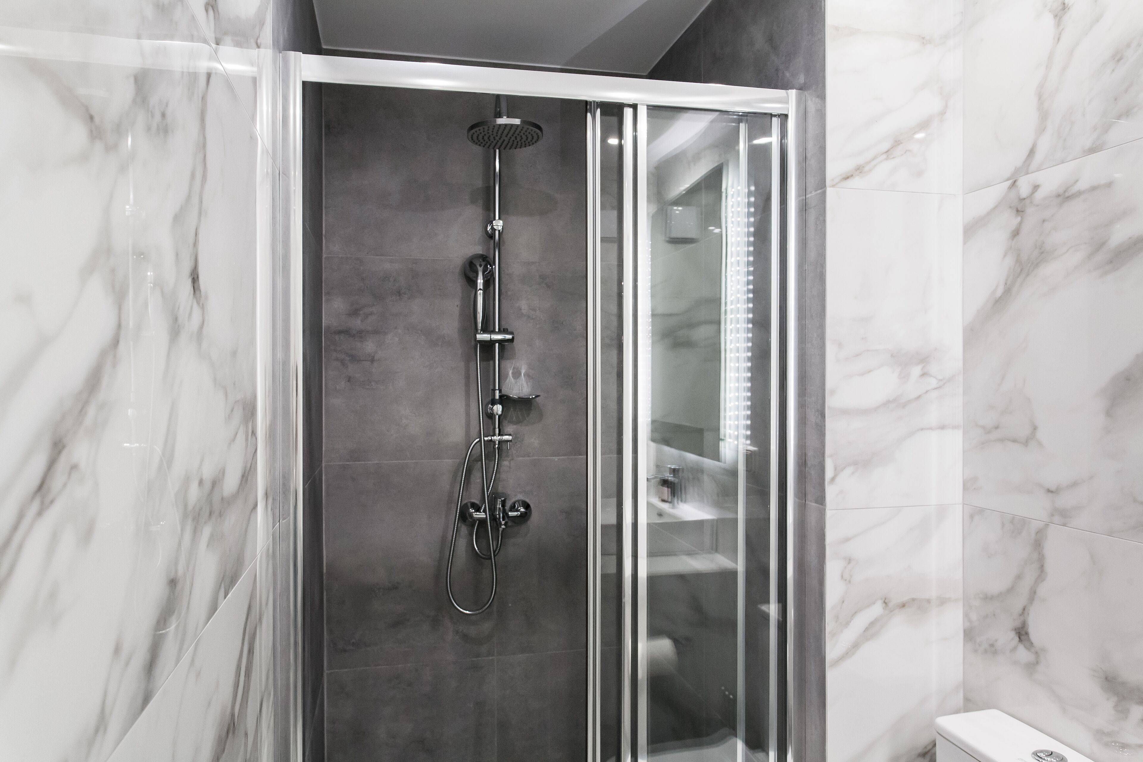 A modern bathroom with a glass-enclosed shower, marble walls, and a visible toilet.