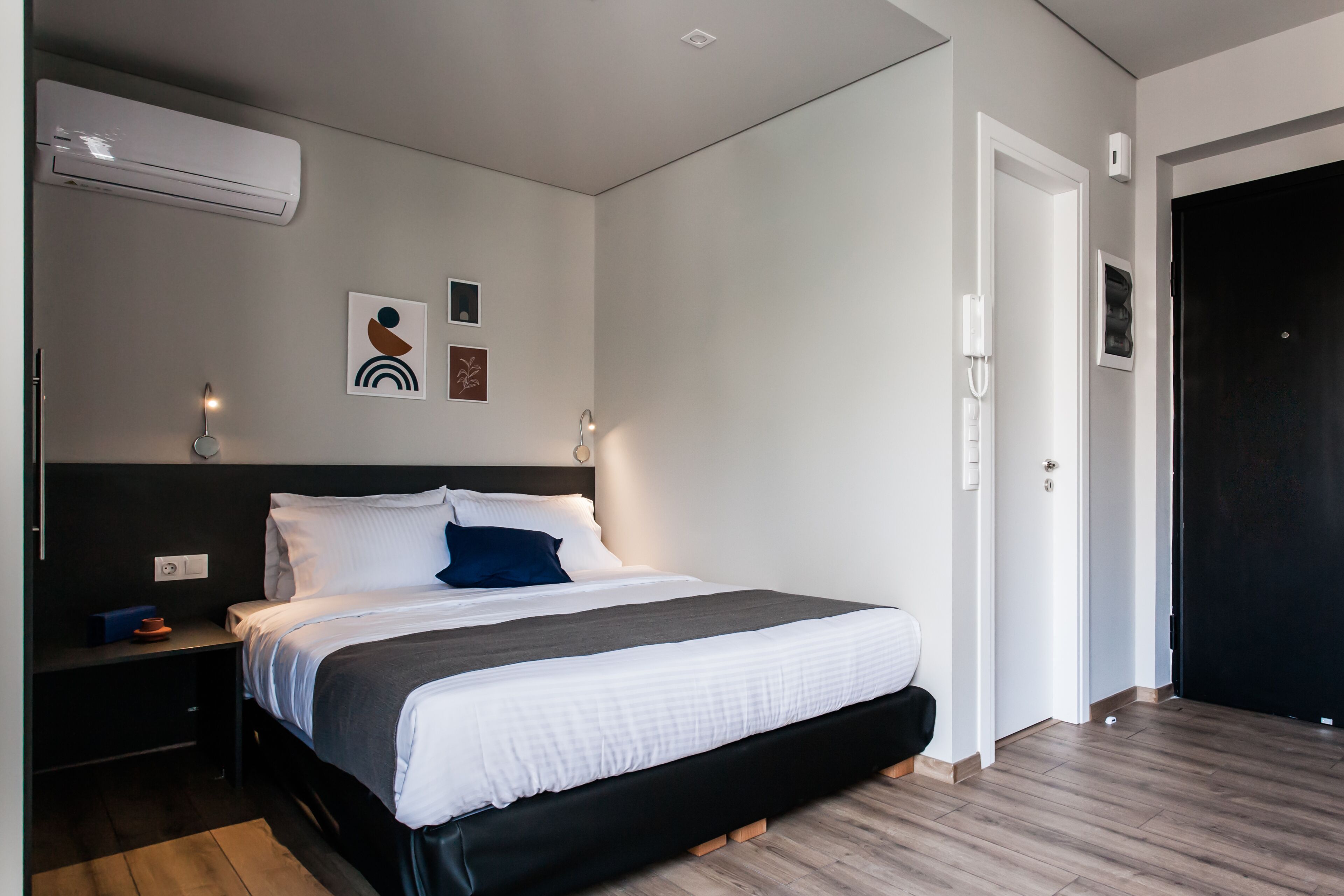 Un dormitorio moderno con una cama grande, una mesita de noche, un aire acondicionado y una puerta.