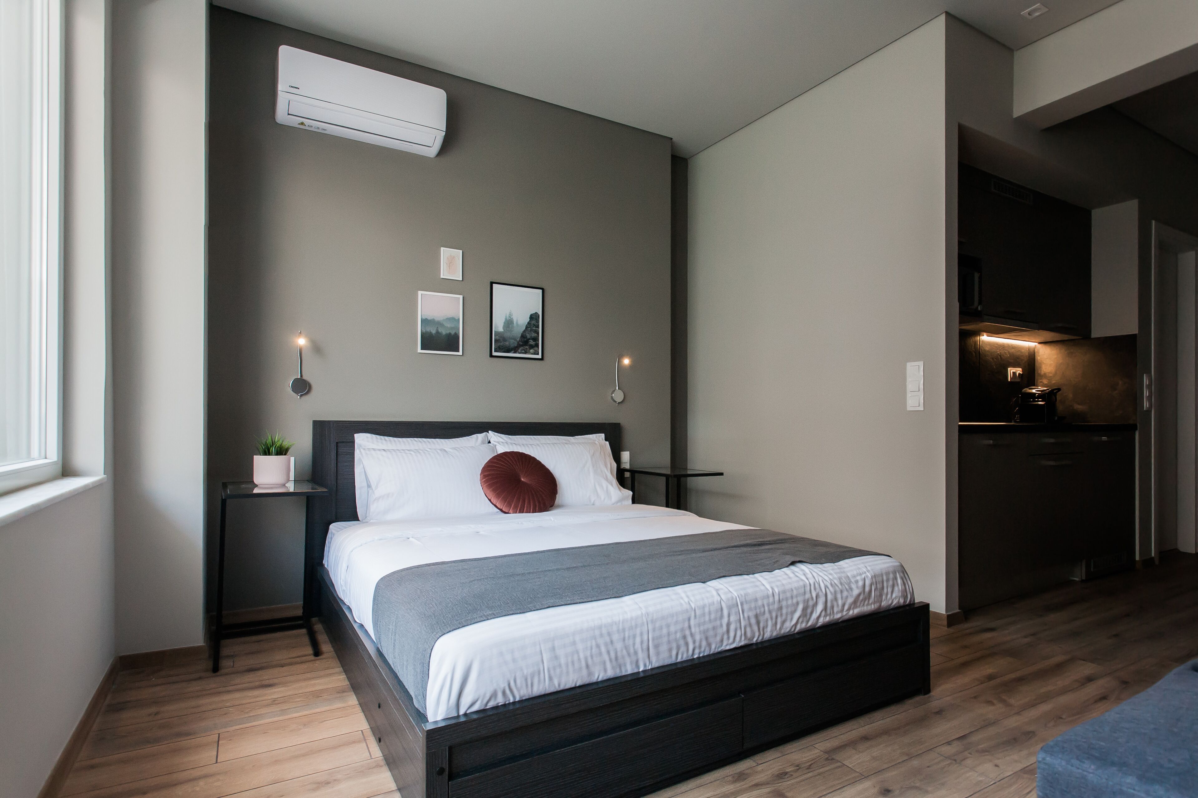 Une chambre à coucher moderne avec un grand lit, des tables de chevet, une petite plante et une vue sur la cuisine.