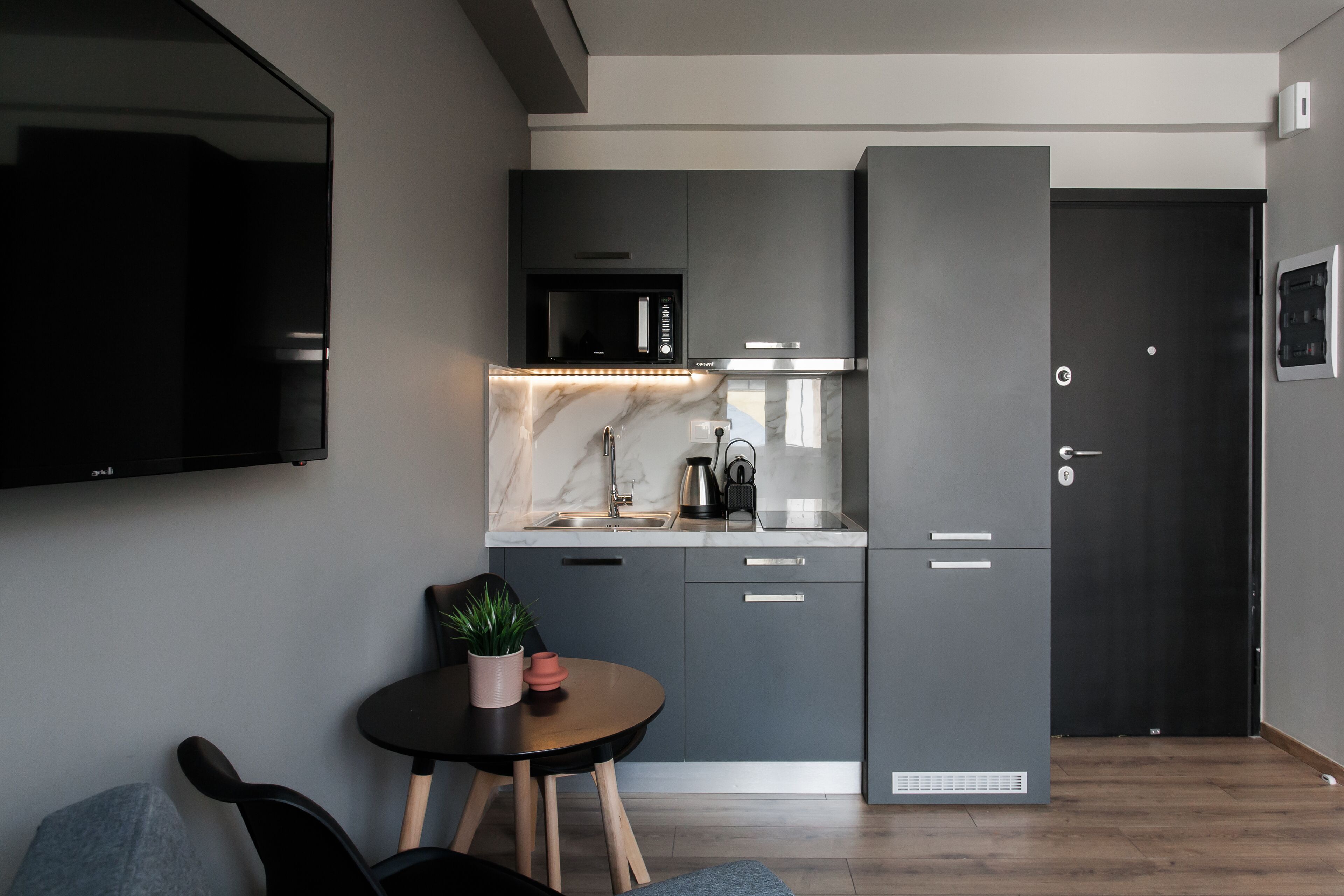A modern kitchen with grey cabinets, a black microwave, and a marble countertop.