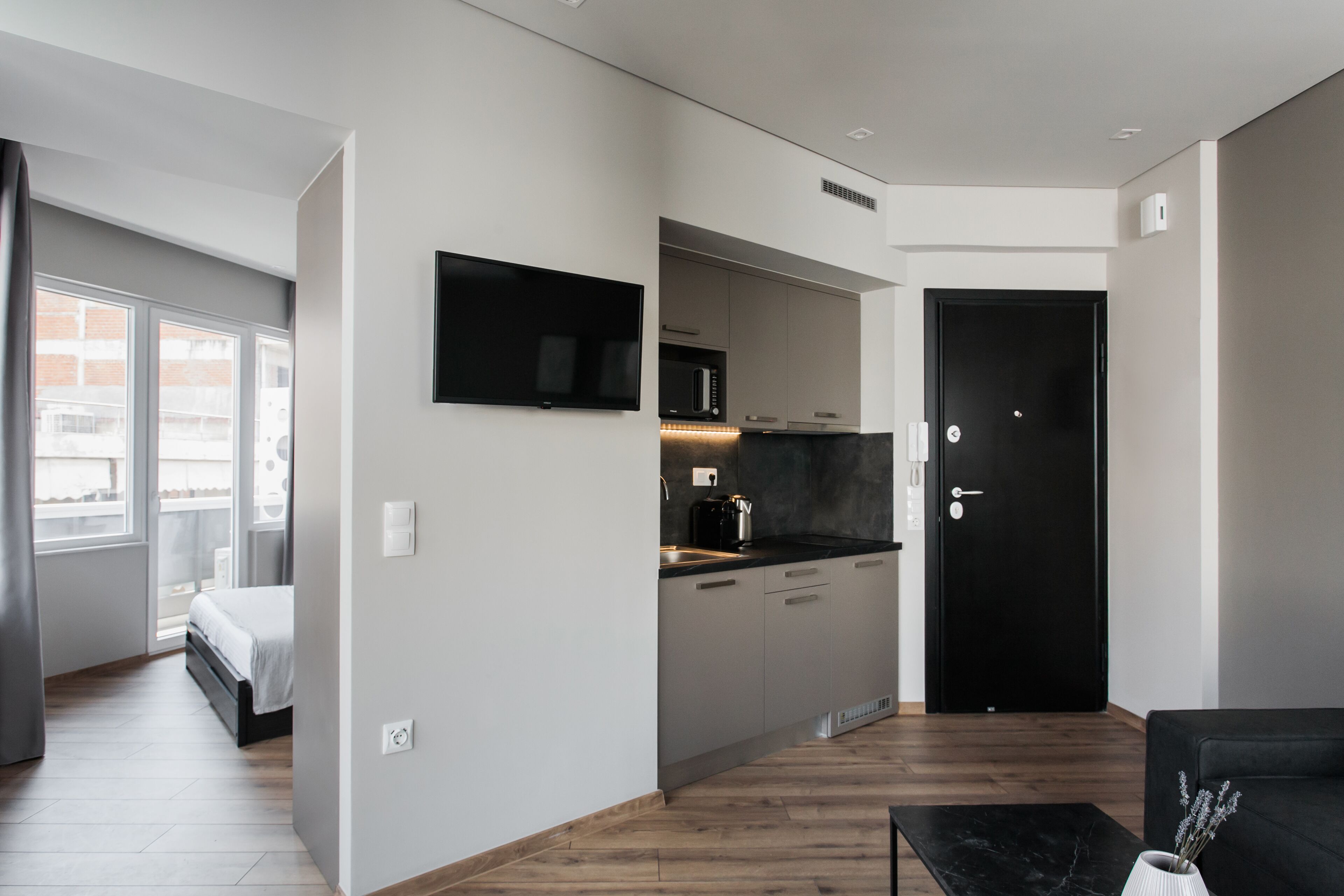 A modern apartment with a kitchenette, a bed, a black sofa, and a dining area.