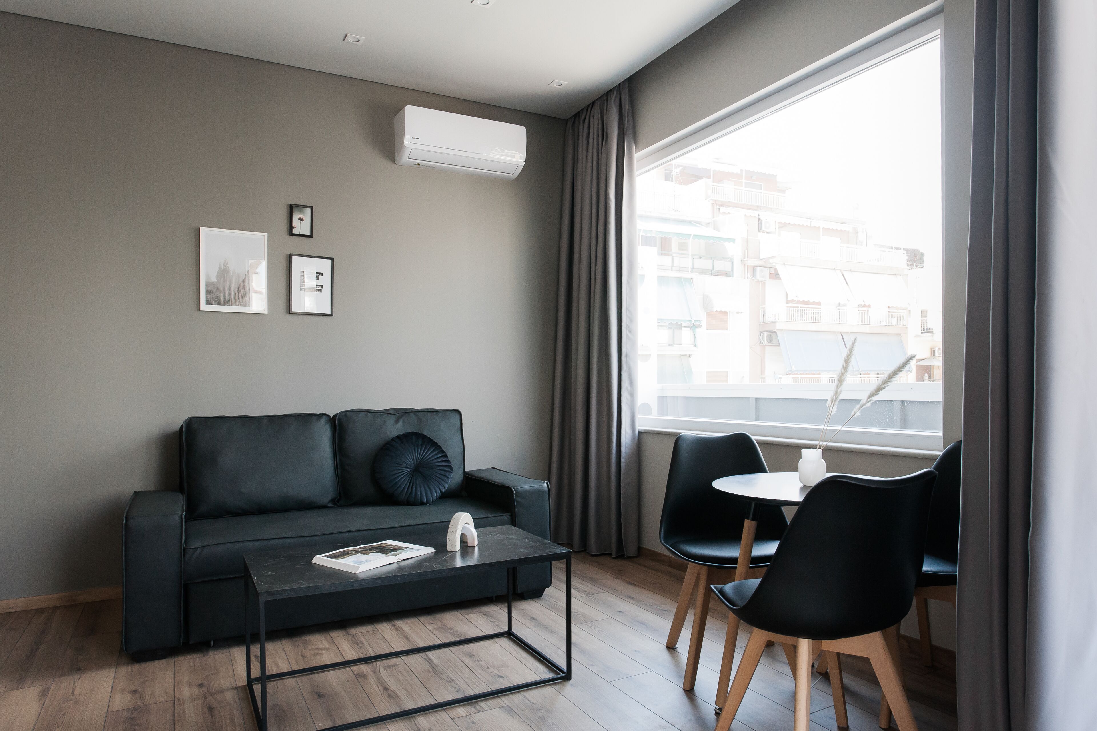 Una sala moderna con un sofá negro, una mesa de centro de vidrio y un comedor con una mesa blanca y sillas negras.