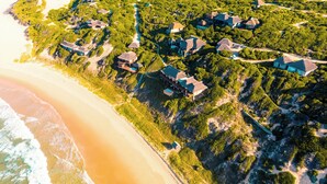 An aerial view of a coastal resort with multiple houses surrounded by dense greenery, a sandy beach, and a clear view of the ocean. - The Beach House at Praia da Rocha (Inhambane)