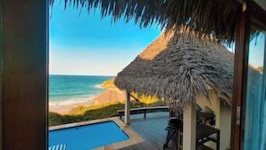 A wooden deck with a pool, a thatched-roof structure, and a view of the ocean. - The Beach House at Praia da Rocha (Inhambane)