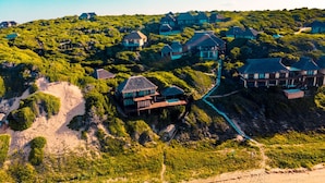 An aerial view of a coastal property with multiple houses, a beach, and a pathway connecting the structures. - The Beach House at Praia da Rocha (Inhambane)