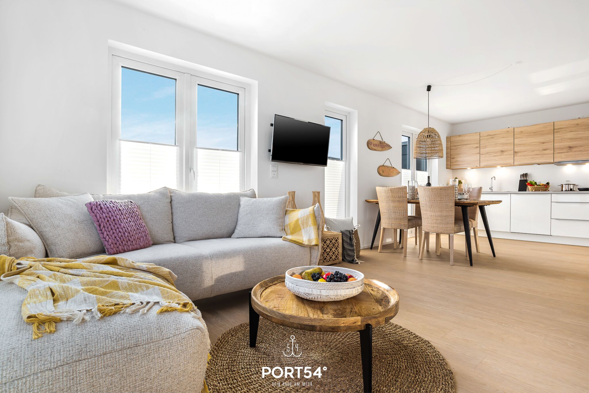 Un salon moderne comprenant un canapé, une table basse ronde avec un panier de fruits, et un coin repas avec des chaises et une table.
