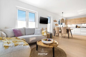 Ein modernes Wohnzimmer mit einer Couch, einem runden Couchtisch mit einer Obstschale und einem Essbereich mit Stühlen und Tisch.