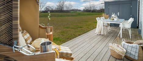 Une terrasse avec une table et des chaises, un canapé en osier et un petit coin jardin.