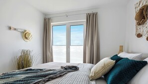 A bedroom with a large bed, a view through a window, and a wall-mounted hat. - Obiza - Baltic Sea, at the harbor, sauna, fireplace, terrace, parking space (Olpenitz)