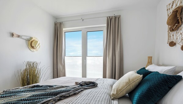 A bedroom with a large bed, a view through a window, and a wall-mounted hat. - Obiza - Baltic Sea, at the harbor, sauna, fireplace, terrace, parking space (Olpenitz)
