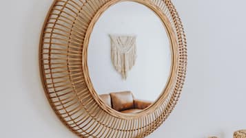 Un espejo redondo tejido en una pared, una mesita de madera con un soporte negro, y una silla tejida.