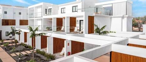 A modern multi-story residential building with a white exterior, wooden accents, and a central courtyard with palm trees.