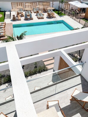 Zona de piscina moderna con sillones de descanso y sombrillas, piscina azul cristalina y barandilla de vidrio.