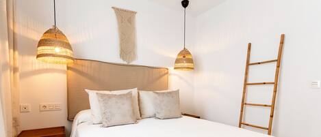A bedroom with a bed, two bedside lamps, a wooden ladder, and a wall-mounted macrame piece.