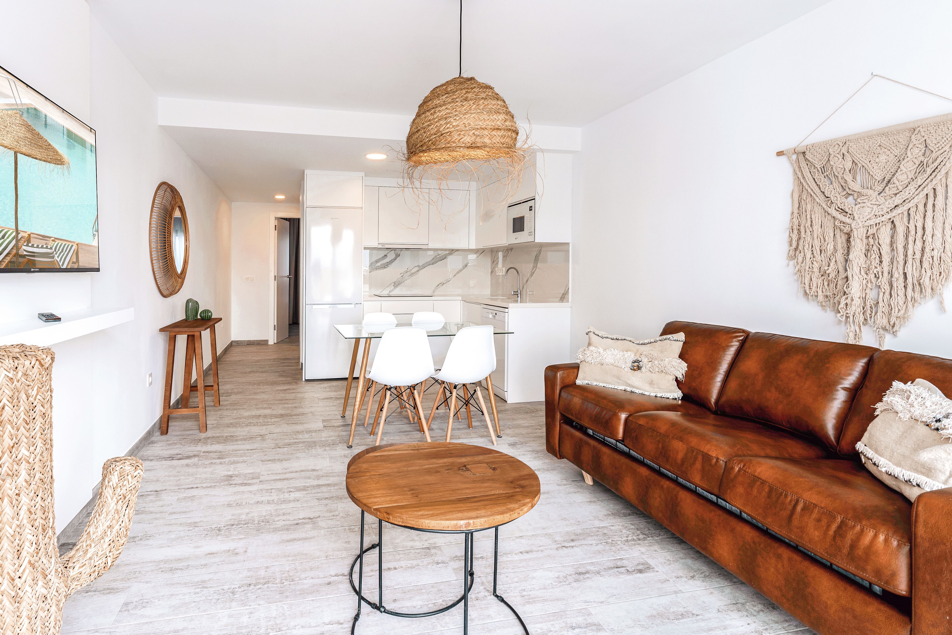 A modern living room with a brown leather sofa, a round wooden coffee table, and a dining area with white chairs.