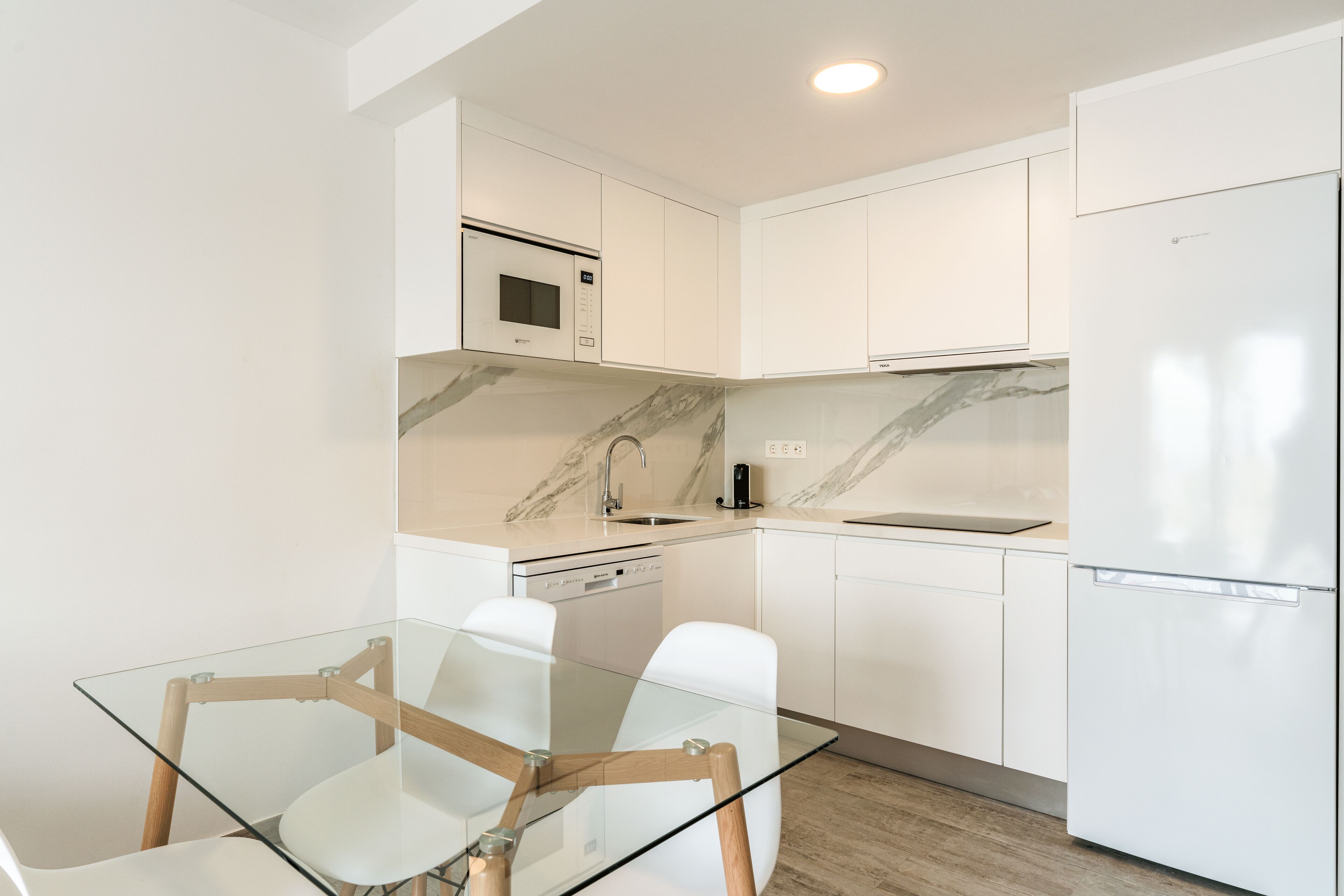 Una cocina moderna con armarios blancos, una mesa de comedor de vidrio y un microondas integrado.