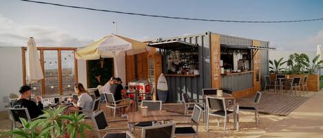 An outdoor seating area with tables and chairs, a bar area, and a view of the landscape.