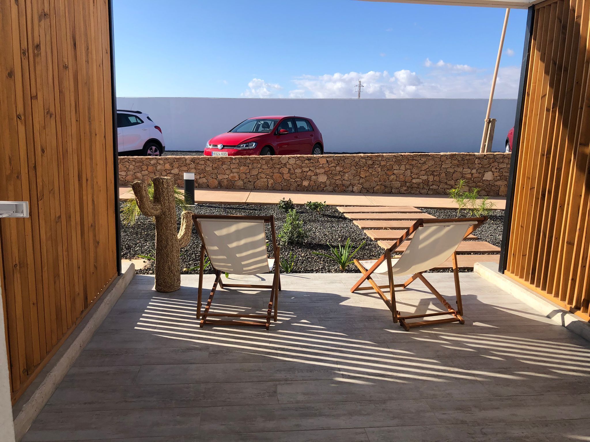 An open patio with two wooden chairs, a cactus decoration, and a stone wall.