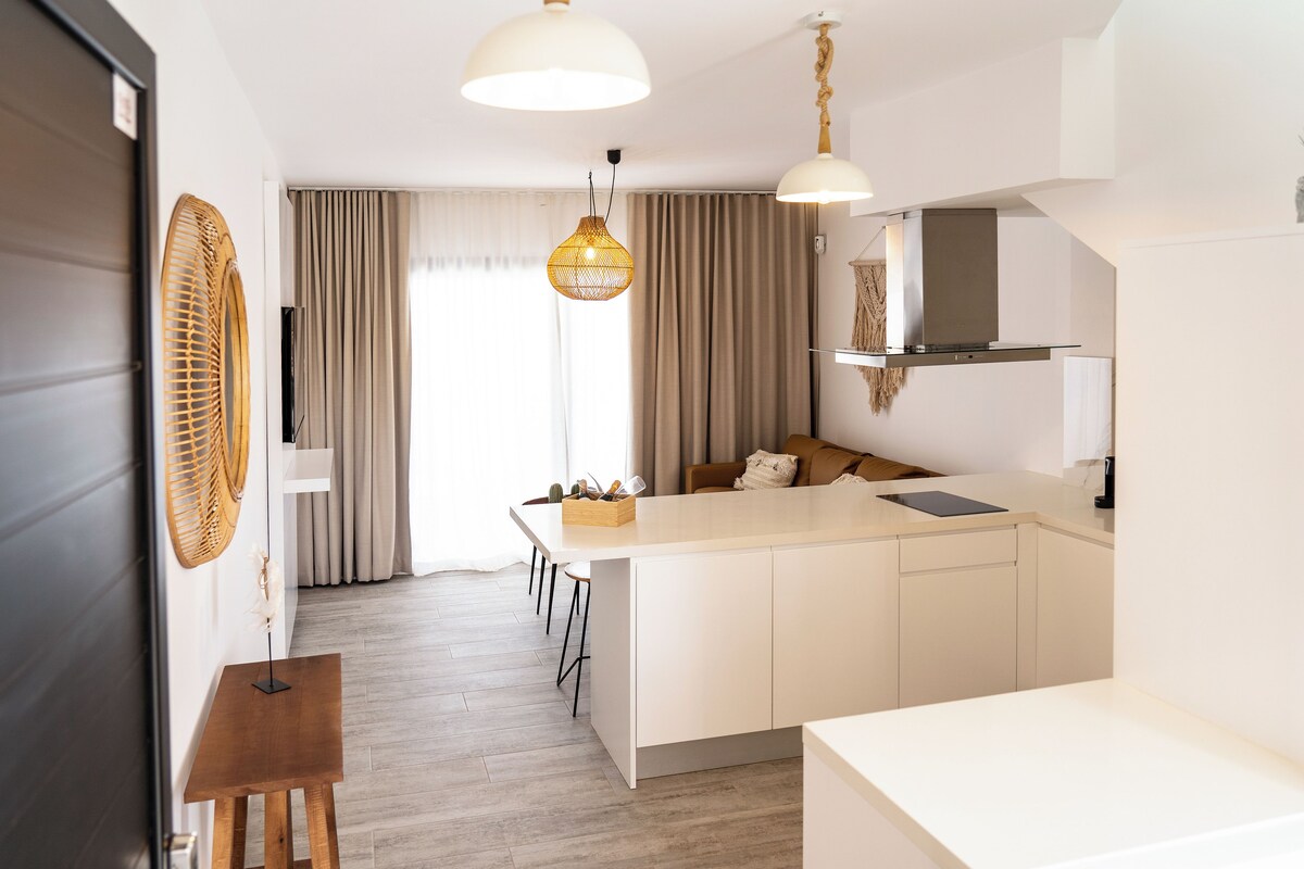 Eine moderne Küche mit einer zentralen Kochinsel, Pendelleuchten und einem Essbereich mit einem Holztisch.