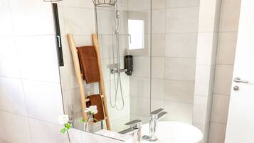 A modern bathroom with a white vanity, two sinks, a shower, and a wooden bench.